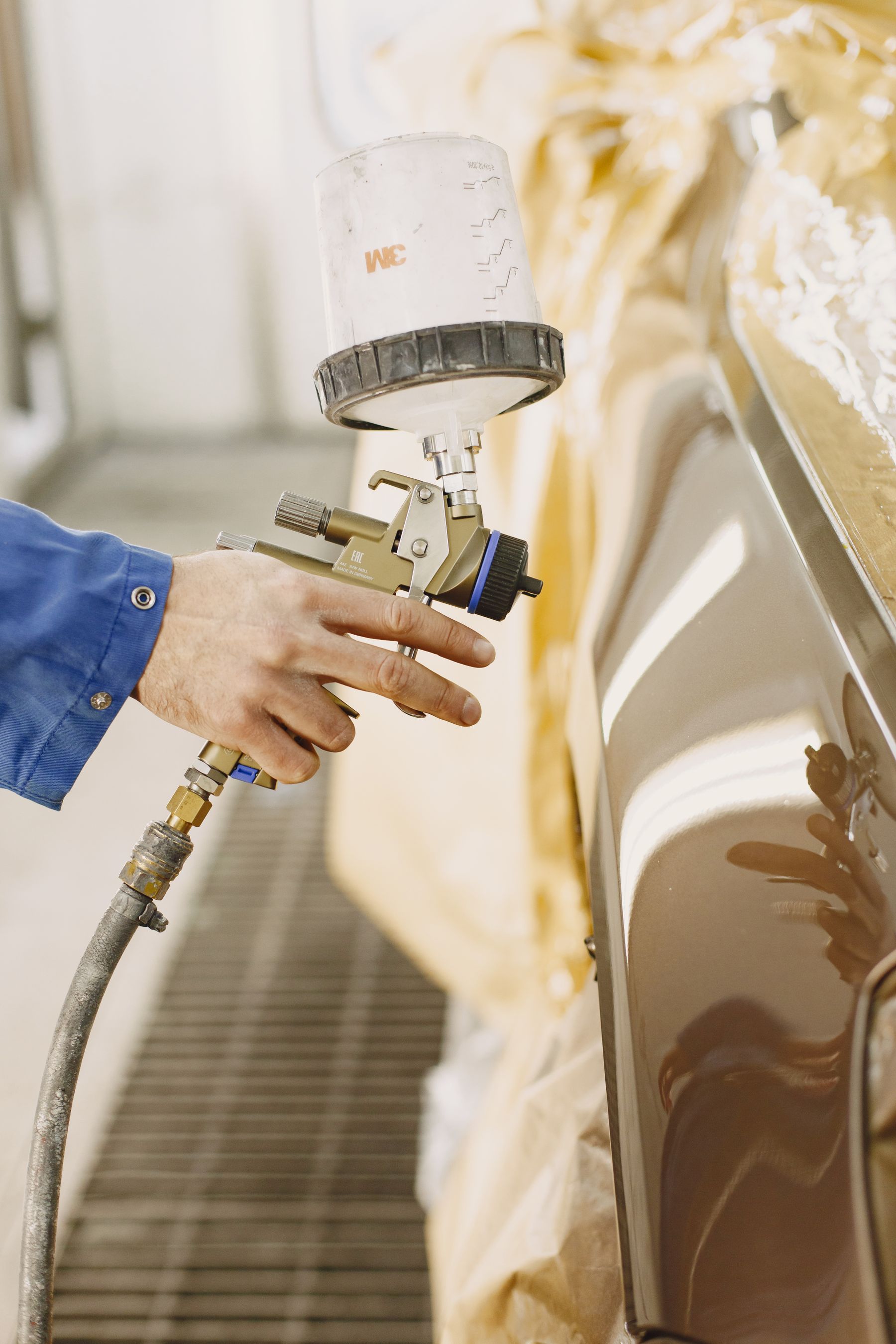A spray gun applying paint to a carefully masked car panel