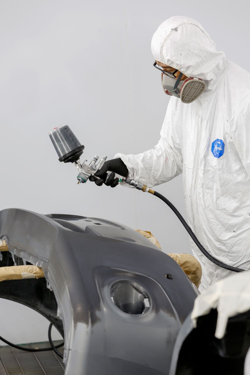 A paint technician in protective clothing spray painting a bumper